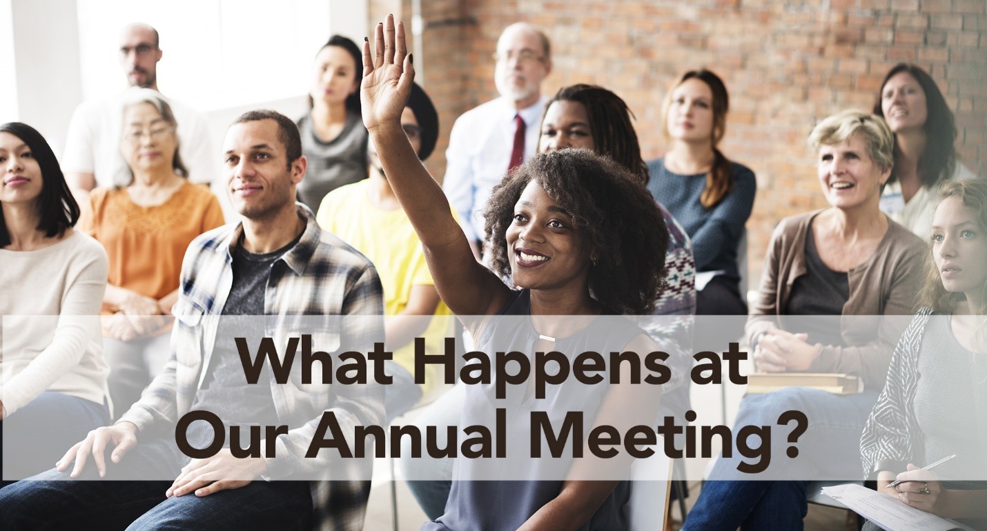 Image of a group of people sitting at a meeting with a woman raising her hand in the front. Text says 'What Happens at Our Annual Meeting?'